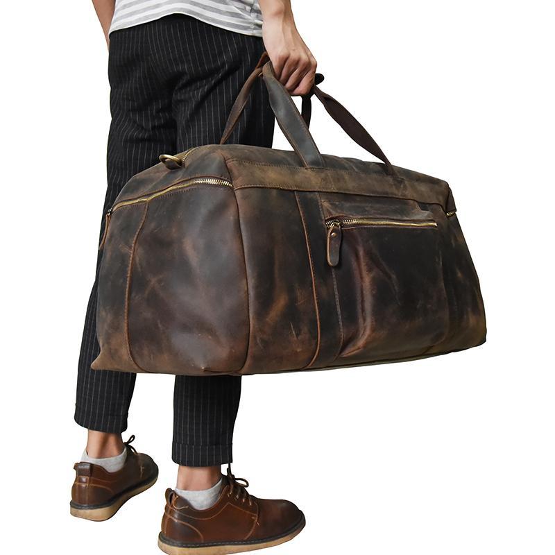 Side view of man wearing black jeans and brown shoes holding the Carter Duffel bag by its handle