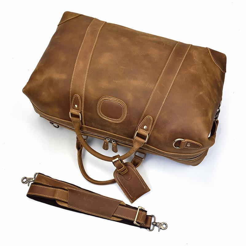 Dayton leather duffle bag on its side with leather shoulder strap next to bag on white background