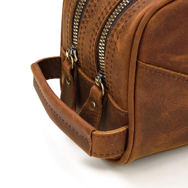 side view of men's toiletry bag showing double zippers with leather tips on white background