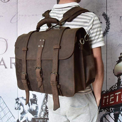 Man with white stiped shirt and beige pants carrying a Cumberland messenger bag with back view of leather straps against a wall  