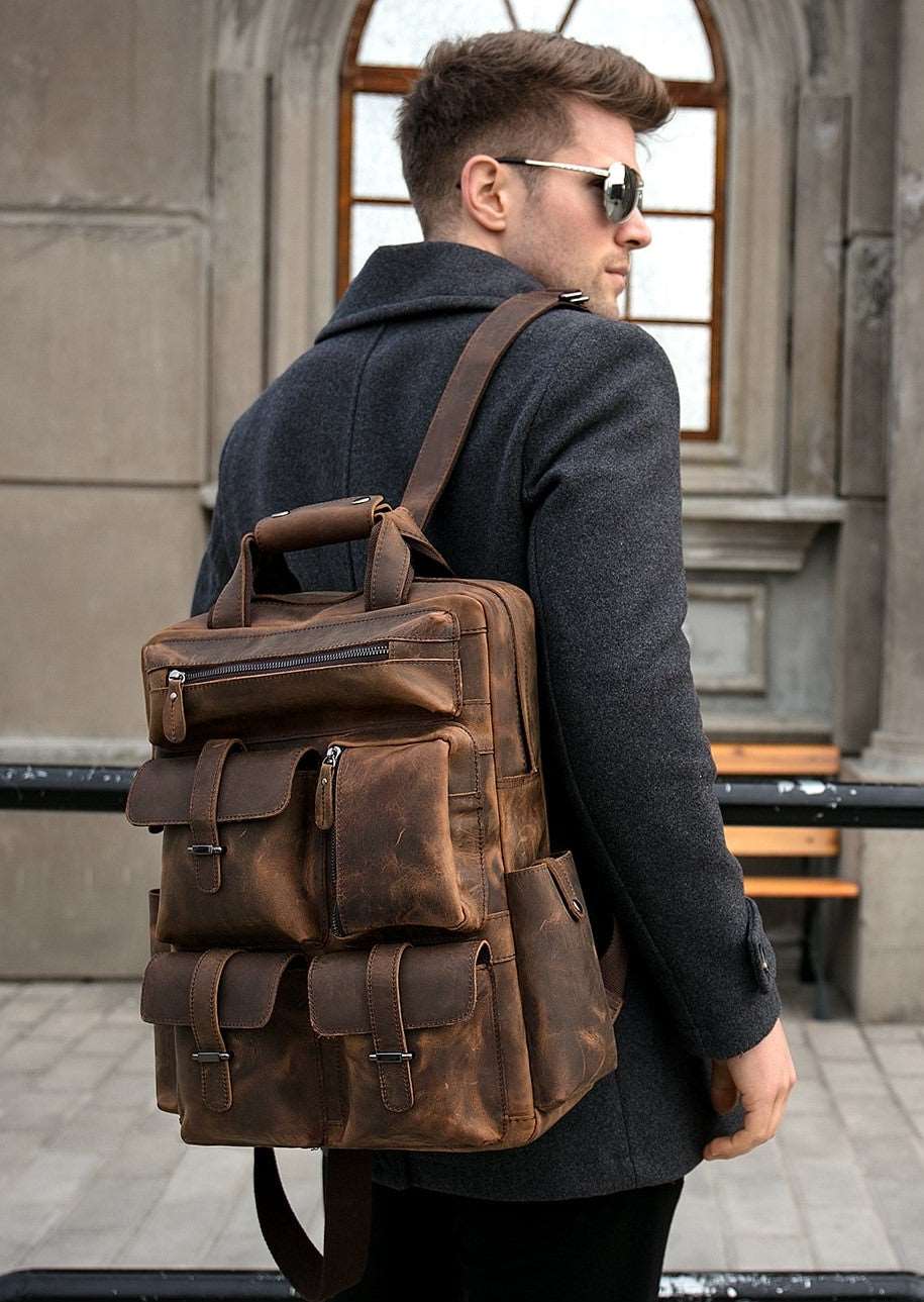 Man with dark colored jacket in in front of building with the Paterson leather backpack over his shoulder showing six different pouches all zippered up