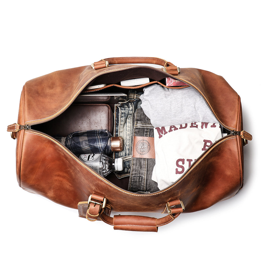 Tan colored weekender Rushmore duffle bag open showing clothes and jeans inside bag on white background