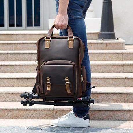 Man with blue jeans and white tennis shoes holding the Yosemite Camera Bag and Lens backpack to his side with tri-pod showing and marble staircase in background